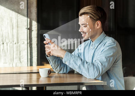 Mobile biometric identification and verification face detection concept. face ID scaning or unlocking technology. young happy man sitting and scanning Stock Photo