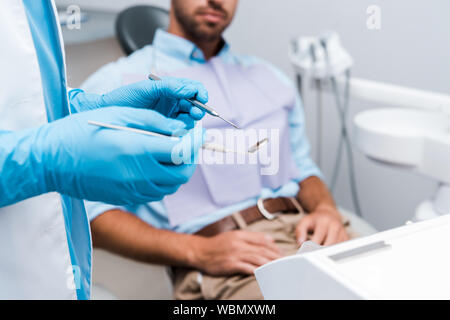 selective focus of dentist in blue latex gloves holding dental instruments near patient Stock Photo