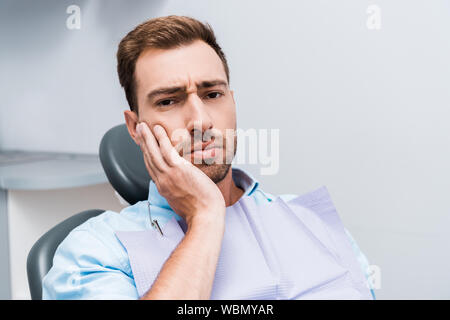 upset bearded man touching face while having toothache in dental clinic Stock Photo