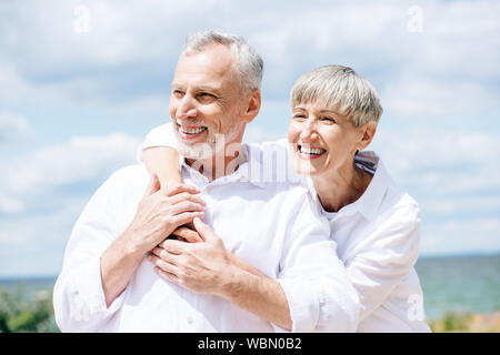 happy senior couple in white shirts embracing under blue sky Stock Photo