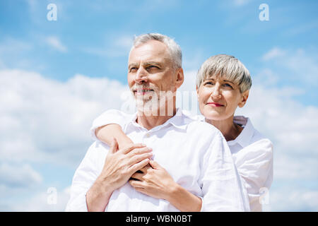 happy senior couple in white shirts embracing under blue sky Stock Photo