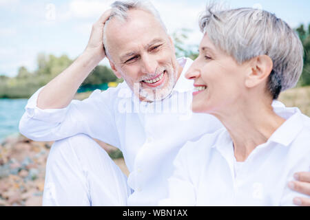 happy smiling senior couple in white shirts embracing under blue sky Stock Photo