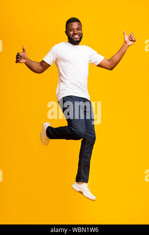 Happy african american man jumping and showing thumbs up Stock Photo