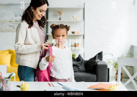 happy mother taking off backpack of cute daughter Stock Photo