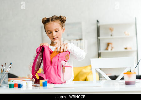 cute schoolgirl putting lunch box in pink backpack Stock Photo