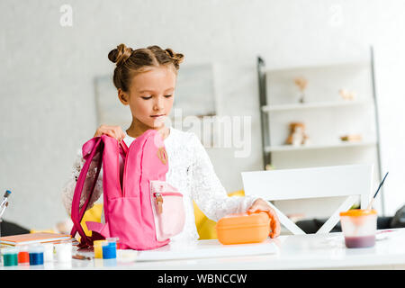 cute schoolgirl holding lunch box near pink backpack Stock Photo