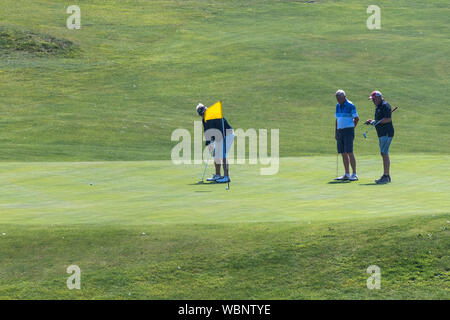 A mature golfer putting on a green as other players watch at Newquay Golf Club in Newquay in Cornwall. Stock Photo