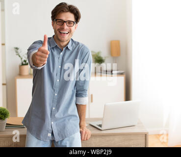 Excited Guy Gesturing Thumbs-Up Standing In Home Office Stock Photo