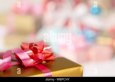 Close up a gold gift box tied with a pink ribbon and a red flower placed on the table. Surprise gifts for special occasions. Select focus shallow dept Stock Photo
