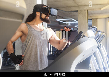 Closeup side view portrait of serious young adult sport man with long curly hair training alone. Handsome male doing exersices in a gym on treadmill a Stock Photo