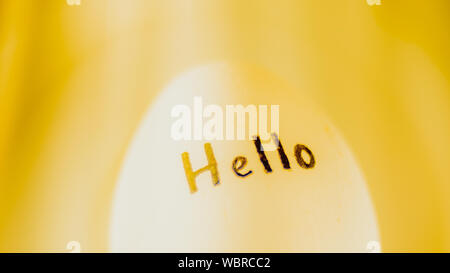 White chicken egg with black inscription Hello, yellow background. Stock Photo