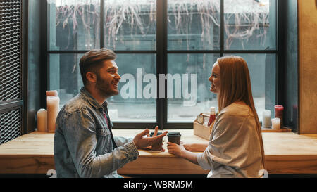 Portrait of two young colleagues talking and laughing as they sit in a cafeteria drinking coffee. Horizontal shot. Side view Stock Photo