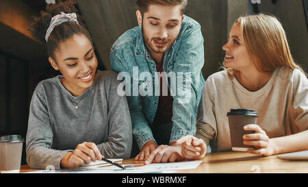 Portrait of three co-workers sharing new ideas with each other as they sit in a cafeteria enjoying a cup of coffee. Charts, diagrams and laptop on the table. Horizontal shot. Front view Stock Photo