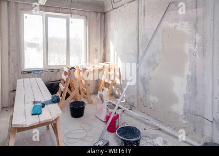 Wooden scaffolding stand near window in empty room, repair, plastering, painting walls, building tools, trash. Concept overhaul of apartment, restruct Stock Photo