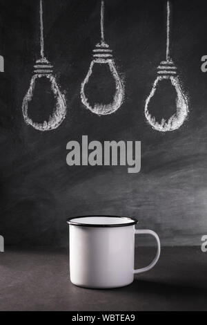 A group of light bulbs sketched in white chalk behind an empty tin mug signifying potential. Stock Photo