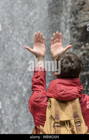 Young man with hands raised towards a waterfall of water Stock Photo