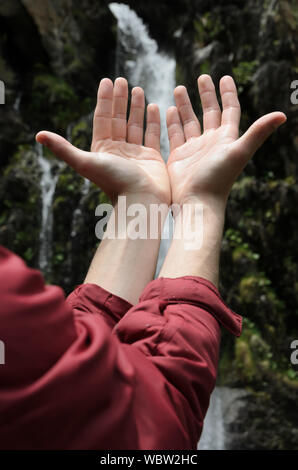 Hands raised towards a waterfall Stock Photo