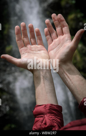 Hands raised towards a waterfall Stock Photo