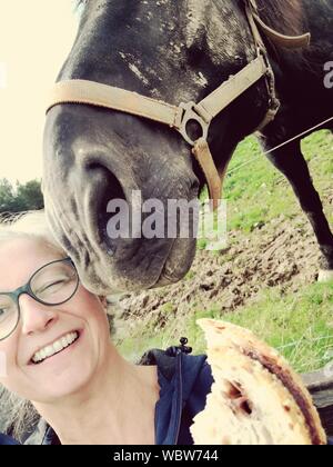 Close-up Portrait Of Happy Mature Woman Feeding Horse On Field