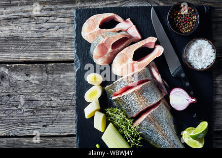 with lime wedges, leek, thyme, salt and spices on a black stone cutting board  on an old rustic wooden table, horizontal view from above, empty space Stock Photo