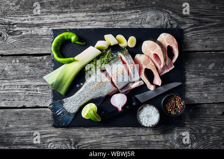 sliced raw fresh trout with lime wedges, leek, thyme, salt and spices on a black stone cutting board  on an old rustic wooden table, horizontal view f Stock Photo