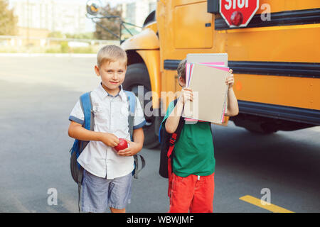Two funny happy Caucasian boys students kids with apples standing near yellow bus on 1 September day. Education and back to school concept. Children p Stock Photo