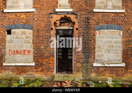 Bricked up windows with danger writing on derelict building UK Stock Photo