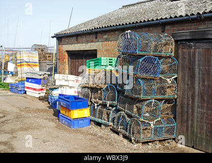 Fish boxes and crab pots stacked by storage sheds at the east end of the harbour at the port of Wells-next-the-Sea, Norfolk, England, UK, Europe. Stock Photo