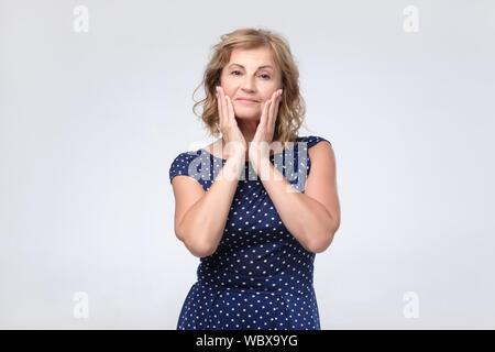 Senior caucasian woman in blue dress touching her face skin. Studio shot Stock Photo