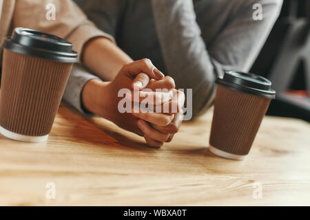 Close up shot of two young women holding each other's hands as they sit in a cafeteria enjoying a cup of coffee. Horizontal shot. Dutch angle Stock Photo