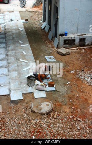 Worker laying stone tiles on the exterior floor in a housing society in Delhi, India Stock Photo