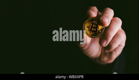 Closeup of golden bitcoin BTC cryptocurrency in hand over dark black background. Man holding golden crypto coin. Virtual money and blockchain concept. Stock Photo