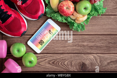 Fitness healthy lifestyle mockup smartphone concept. Get Fits Don't Quit quote on mobile phone with sport shoes, dumbbells and fruits. Mock up mobilep Stock Photo