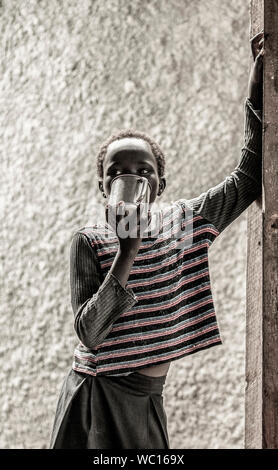 BOR, SOUTH SUDAN-NOVEMBER 4, 2013: An unidentified South Sudanese girl drinks from a tin cup in Bor, South Sudan Stock Photo