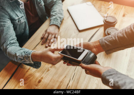 Cropped view of a person paying bill through smartphone using NFC technology in cafe. Horizontal shot Stock Photo