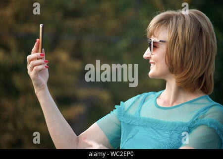 Adult middle-aged business woman on the street makes selfie on smartphone, selective focus Stock Photo