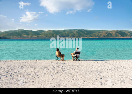 Salda lake like Maldives with white sand and turquoise colored water. One Couple sitting on portable chairs near the waters edge. Burdur / Turkey. Stock Photo