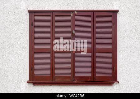 Brown wooden slat window shutters set in a rough cast wall Stock Photo
