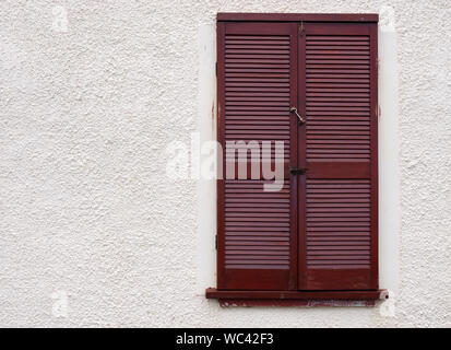 Brown wooden slat window shutters set in a rough cast wall Stock Photo