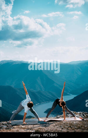 Strong and flexible young couple doing yoga workout. Man and woman on mountain practicing pair yoga in morning