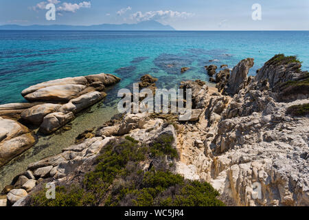 Exotic Platanitsi beach in Sarti, Sithonia, Greece with crystal clear water and spectacular shapes of rocks and mount Athos in background Stock Photo