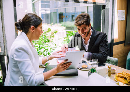 Male and female business partners sitting in cafe and discussing contract while using digital tablet Stock Photo