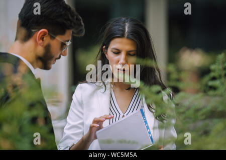 Preparing for meeting. Two young business people walking outside on the city street reading through documents Stock Photo