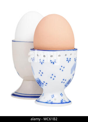 side view of two boiled eggs in ceramic egg cups isolated on white background, the brown egg on foreground Stock Photo