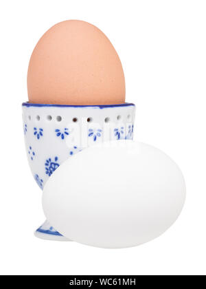 side view of brown boiled egg in ceramic egg cup and white egg isolated on white background Stock Photo