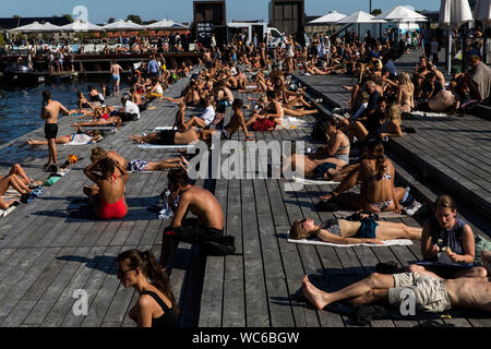Copenhagener and tourists at the wooden pier at Ofelia Square near The Royal Play House and the  historic Nyhavn in Copenhagen, Denmark.  The water in Copenhagen harbor is so clean that it is safe to take a dip. In 2018 Copenhagen topped CNN’s list for “Best Cities for swimming”. Stock Photo