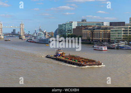 A large barge in the Pool of London on the River Thames with a view of the iconic Tower Bridge and HMS Belfast, viewed from London Bridge