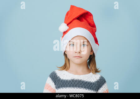 Portrait of cute little first grader girl in a santa's hat and knitted sweater. Stock Photo