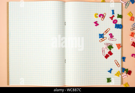open notebook with white sheets in a cage and small multi-colored wooden letters, back to school, copy space Stock Photo