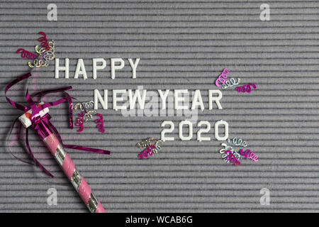 Happy New Year 2020 on grey felt ribbed letter board with white letters and pink confetti and noise maker Stock Photo